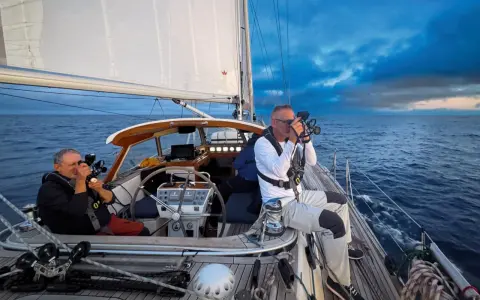 Leon Schulz und ein Kollege filmen auf See. Die Segel sind gesetzt, die Wellen schlagen gegen das Boot.
