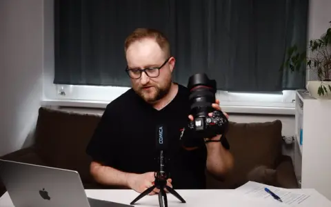 Mężczyzna prezentuje aparat fotograficzny, omawiając elementy kursu fotografii dla początkujących.