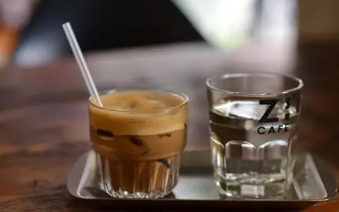 Kawa z lodem i słomką obok szklanki wody. Czy kawa jest moczopędna? Z's Cafe.
