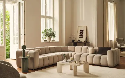 Ampio divano componibile color crema, dalle forme morbide e arrotondate, perfetto per definire le dimensioni di un salotto moderno.