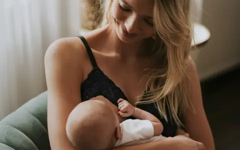 Uśmiechnięta mama karmi piersią swoje dziecko. Delikatne chwile bliskości i miłości.
