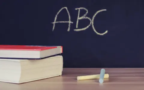Libri e gessetti su un tavolo di legno, con la scritta "ABC" su una lavagna scura. Un'immagine che evoca l'inizio di nuovi percorsi di apprendimento, come i **corsi abilitanti**.