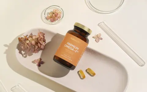 Butelka z suplementem omega 3 dla niemowląt, dwie kapsułki i suszone kwiaty na ceramicznej tacce.