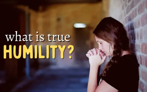 A woman with her hands clasped in prayer leans against a brick wall, contemplating "what is true HUMILITY?".