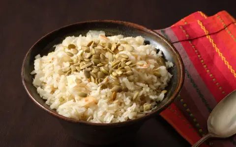 Un tazón de arroz de coco con semillas de calabaza y coco rallado, servido sobre una servilleta colorida.
