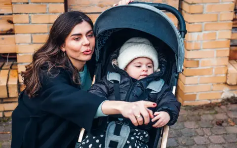 Mama pokazuje coś dziecku w najmniejszej spacerówce. Maluch w czapce i kurtce wygląda ciekawie.