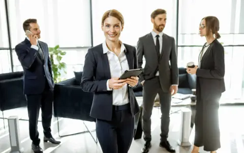 Une femme souriante, possiblement le chief of staff, tient une tablette. Autour d'elle, des collègues en costume discutent dans un bureau moderne.
