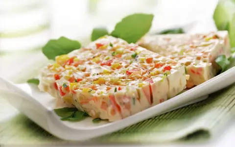 Tranches de terrine de légumes colorée, garnie de feuilles vertes, sur une assiette blanche.