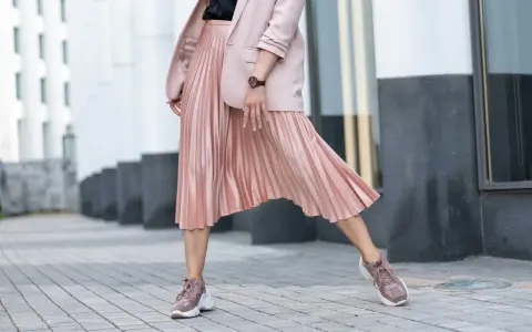 Kobieca stylizacja: różowa plisowana spódnica, marynarka i sportowe buty. Idealne połączenie elegancji i wygody, pokazujące, jakie buty do plisowanej spódnicy pasują najlepiej.