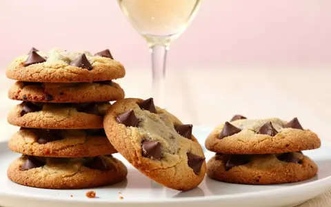 Gestapelte, goldbraune American Cookies mit Schokoladenstückchen und ein Glas Sekt.