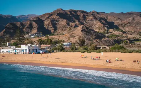 Słoneczne gran canaria plaże z piaszczystym brzegiem, turkusową wodą i górami w tle. Ludzie odpoczywają pod parasolami.