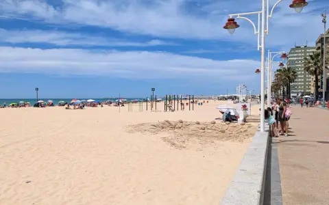 Sonniger Tag am Playa Victoria in Cádiz. Menschen entspannen sich unter bunten Sonnenschirmen, während Kinder am Strand spielen.