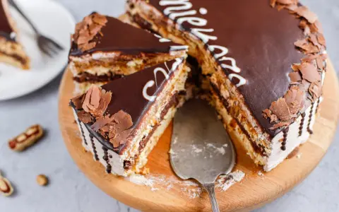 Pyszny tort snickers bez pieczenia, udekorowany czekoladą i wiórkami. Idealny na deser!