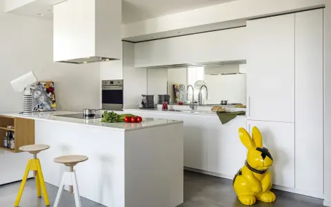 Cucina moderna con isola centrale e sgabelli. La differenza tra RAL 9003 e 9010 è sottile, ma qui il bianco puro domina, con un tocco di giallo dato da un coniglio decorativo.