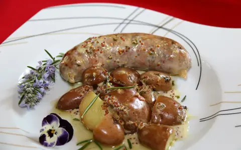 Une andouillette sauce moutarde, accompagnée de pommes de terre grenaille et garnie de romarin et d'une pensée.