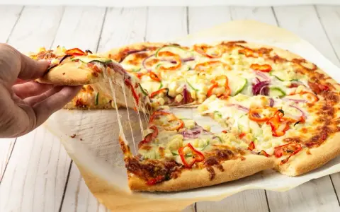 Pyszna pizza domowa z ciągnącym serem, papryką, cebulą i cukinią. Ktoś właśnie podnosi kawałek.