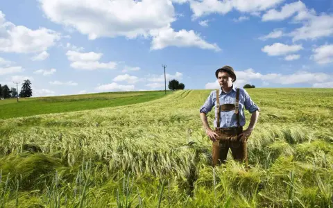 Un homme en culotte de peau et chapeau se tient dans un champ d'orge. Son nom, Hoffmann, pourrait avoir une origine juive, évoquant une histoire ancestrale.