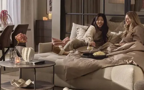 Två vänner myser i en stor sov fåtölj med popcorn och filtar.