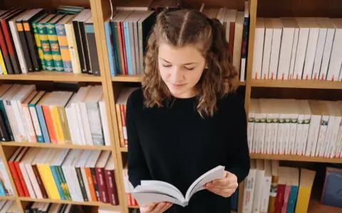 Dziewczynka z warkoczykami czyta książkę na tle regałów pełnych literatury. Może to być streszczenie "Skarbczyka" lub innej lektury.