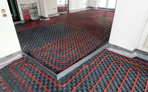 Instalación de un sistema de calefacción por suelo radiante, con tuberías rojas serpenteando sobre una base negra. Preparando un suelo refrescante para el confort.