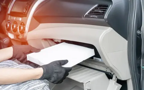 Wymiana filtra kabinowego w Audi A3 8L. Ręce w rękawiczkach wyjmują biały filtr z wnętrza schowka.