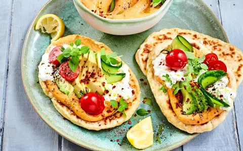 Leckere kalte gerichte ohne kochen: Fladenbrot mit Hummus, Avocado, Tomaten, Gurke und Frischkäse. Garniert mit Kräutern und Zitrone.