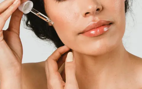 Une main applique une goutte d'huile de ricin visage sur la peau. Les lèvres sont brillantes, la peau est lumineuse.