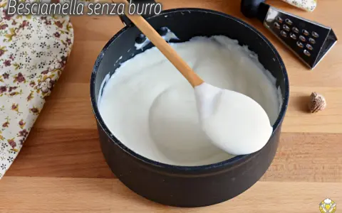 Besciamella senza burro cremosa in pentola, pronta per condire i tuoi piatti. Un cucchiaio di legno la raccoglie.