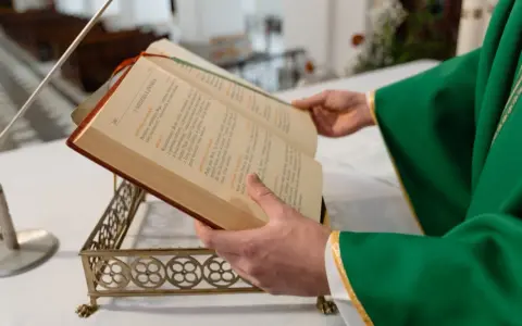 Kapłan w zielonej szacie czyta księgę podczas mszy żałobnej.