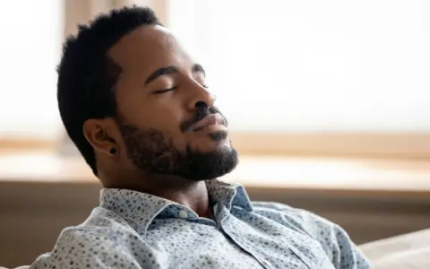 A man with closed eyes and a beard breathes deeply, finding a moment to ground himself amidst the day's chaos.