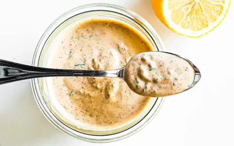 En sked krämig remouladsås med örter lyfts ur en burk. Bredvid ligger en halv citron. Perfekt för ditt remouladsås recept!