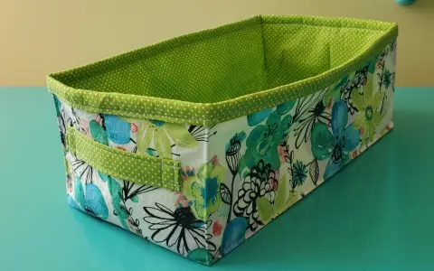 Panier rectangulaire en tissu, doublé de pois verts. Son extérieur est orné d'un motif floral coloré, parfait pour ranger vos affaires avec style.