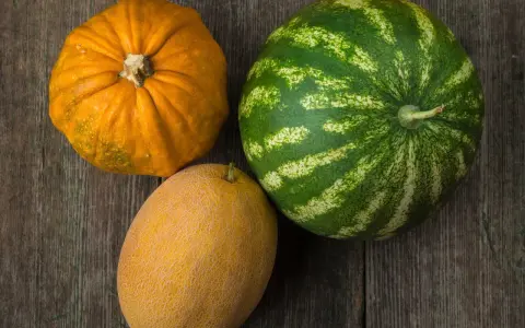 Dynia, melon i arbuz leżą na drewnianym blacie.
