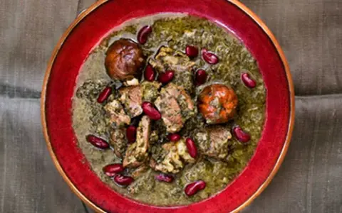 En skål med ghorme sabzi, en mustig persisk gryta med kött, örter och röda bönor, serverad i en röd kantad skål.
