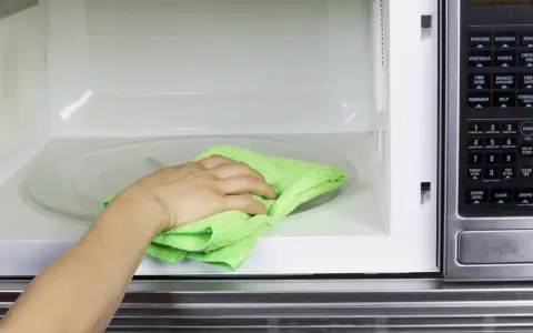 Mano con paño verde limpiando el interior de un microondas.