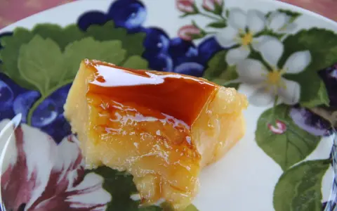 Un trozo de tocino de cielo de la abuela, con su caramelo brillante, sobre un plato decorado con flores y frutos.