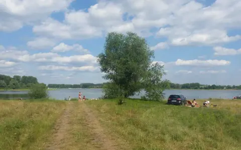 Słoneczny dzień nad jeziorem przeczyckim. Ludzie odpoczywają na trawie, w tle widać wodę i drzewa.