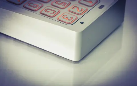 Zbliżenie na klawiaturę domofonu z podświetlanymi na pomarańczowo przyciskami z cyframi.