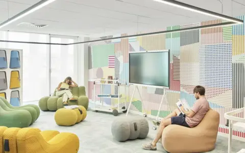 Un espace de repos coloré avec des poufs confortables et un mur à motifs géométriques. Deux personnes lisent tranquillement.