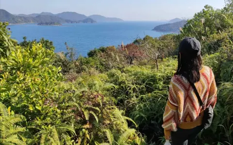 Frauen genießen die Aussicht beim Hong Kong Hiking. Grüne Vegetation und das blaue Meer erstrecken sich bis zu den Hügeln.
