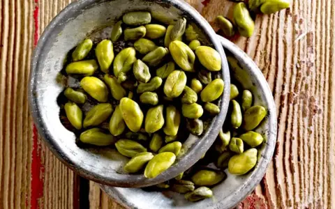 Grüne Pistazienkerne in zwei Schalen auf Holzuntergrund. Diese gesunden Pistazien sind ein leckerer Snack.