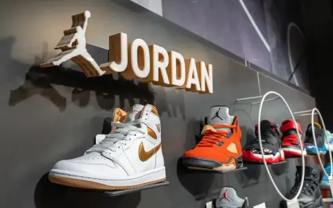 Na wystawie butów Jordan, białe Air Jordan 1 z złotymi akcentami. Obok pomarańczowe Air Jordan 5. Czy 8 5 jaki to rozmiar buta?