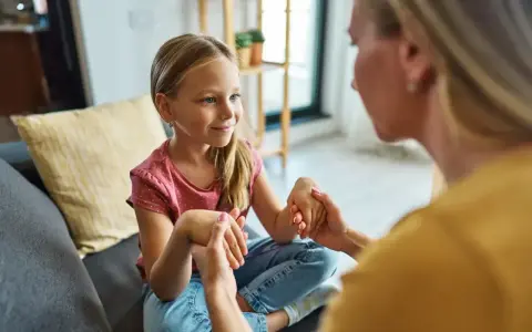 Mama spokojnie tłumaczy córce, jak rozmawiać z dzieckiem o złym zachowaniu. Dziecko słucha uważnie, trzymając dłonie mamy.