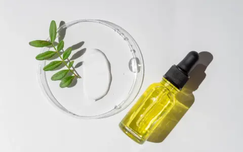 Kropla białego kremu i żółte serum w buteleczce z pipetką, obok gałązka z liśćmi. Składniki do walki z trądzikiem, w tym retinoidy na trądzik.
