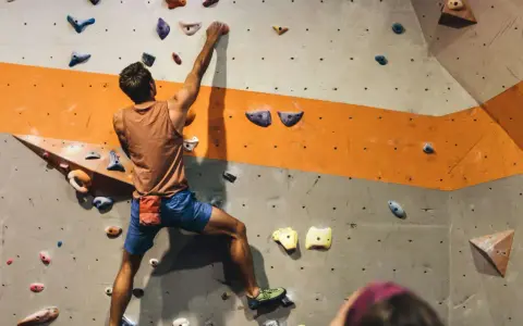 Mężczyzna wspina się po ścianie z kolorowymi chwytami. To właśnie bouldering – wspinaczka bez liny na niskich ściankach.