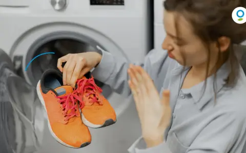 Woman holding smelly orange sneakers near an open washing machine.