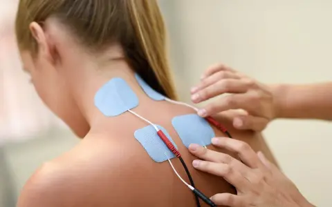 Elektrody na plecach kobiety podczas terapii fizykalnej. Terapeuta przygotowuje do zabiegu.