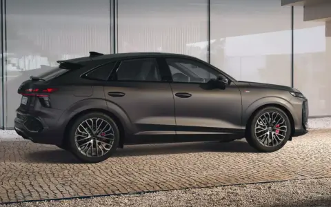 Elegancki Audi Q3 2025 w ciemnym kolorze, z dynamiczną linią nadwozia, prezentuje się na tle nowoczesnej architektury.