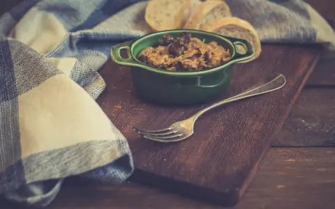Pyszny bigos z szybkowaru w zielonej miseczce, obok kromki chleba i widelca.
