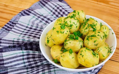 Młode ziemniaki w misce, posypane koperkiem i szczypiorkiem. Idealne na lato, a ile gotować młode ziemniaki? Krótko!